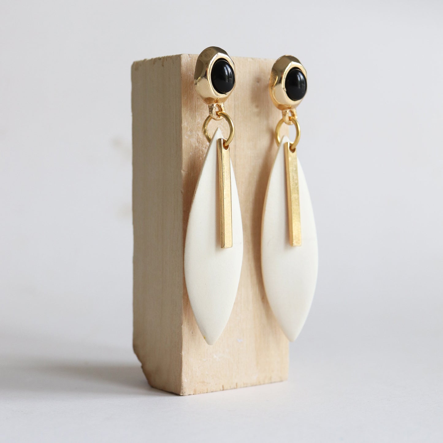 Pendientes largos de cerámica blanca y detalles dorados, con perlas negras, estilo moderno y elegante.
