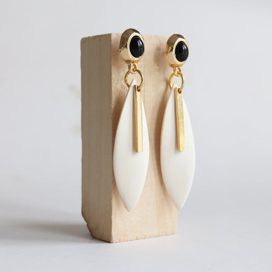 Pendientes largos de cerámica blanca y detalles dorados, con perlas negras, estilo moderno y elegante.