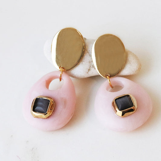 Pendientes de resina rosa con detalles dorados y gema negra, estilo moderno y elegante.