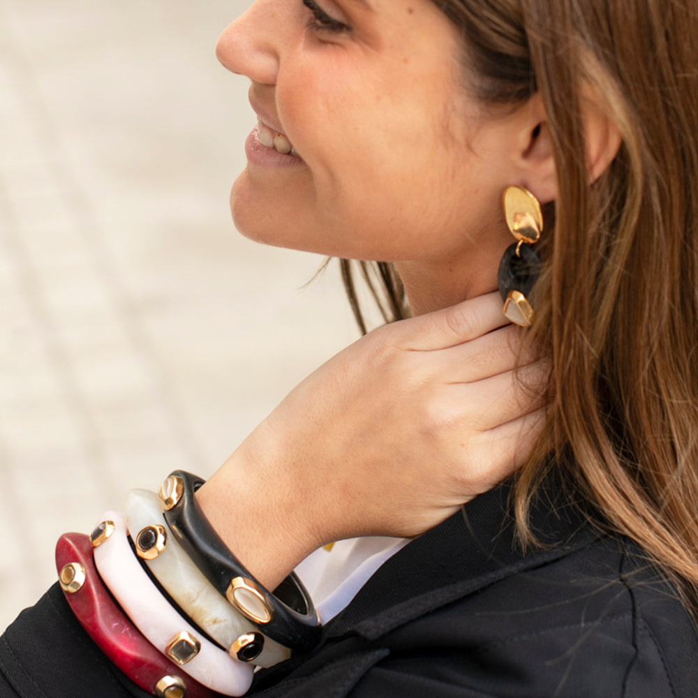 Pulseras de acrílico en rojo, blanco y negro con detalles dorados, y aretes elegantes a juego.