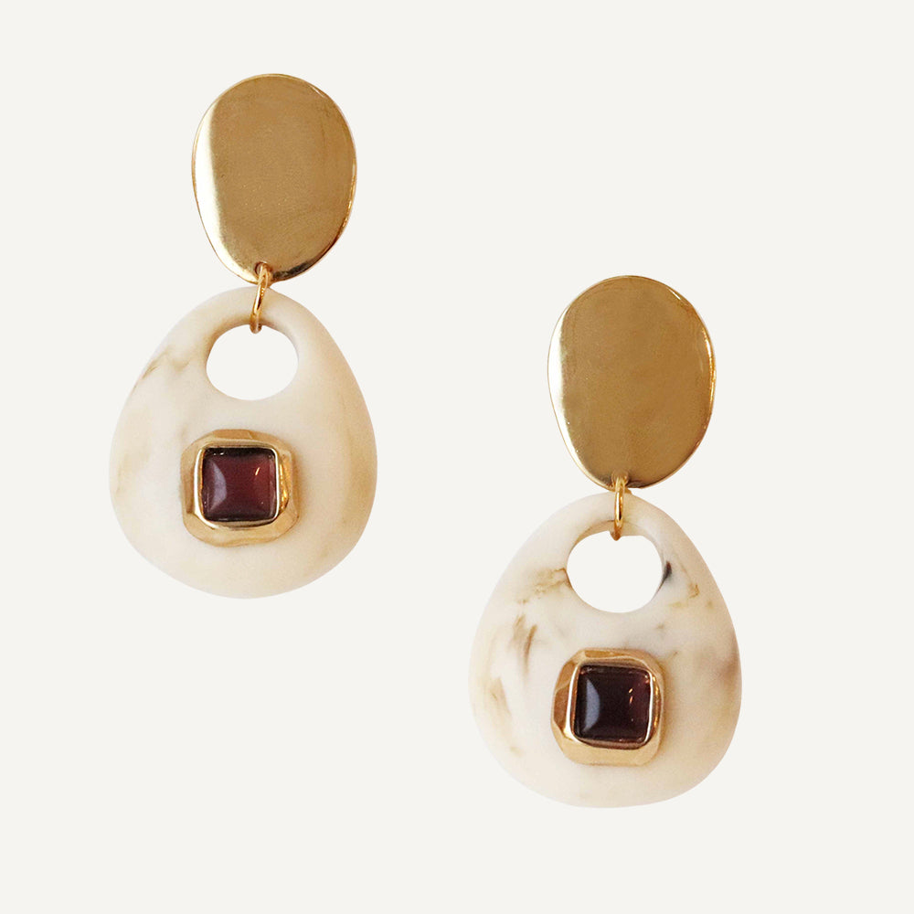 Pendientes de resina blanca con detalles en dorado y piedra granate, estilo moderno y elegante.