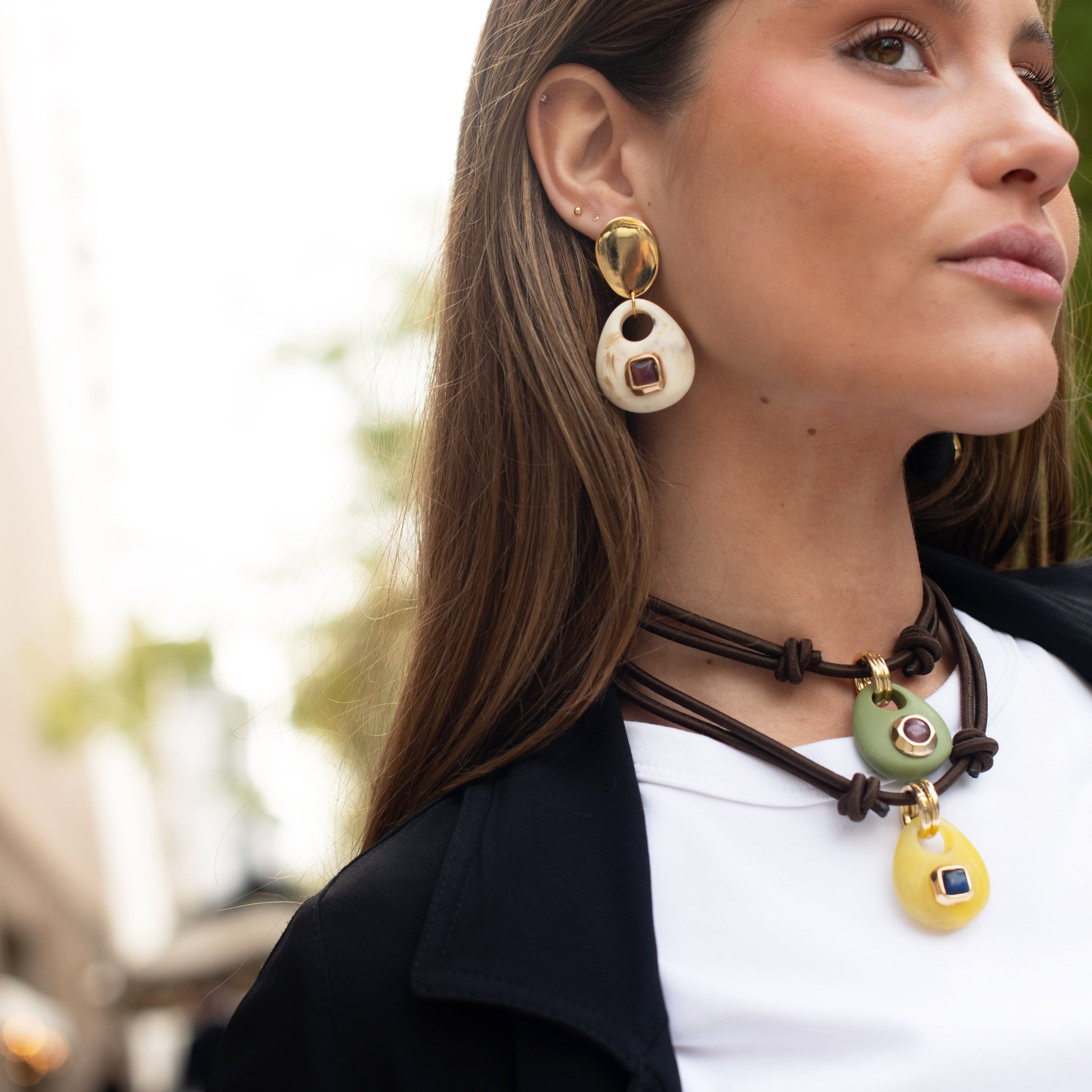 Collar de cuero marrón con colgantes amarillos y verdes, y pendientes grandes en tonos crema y dorado.