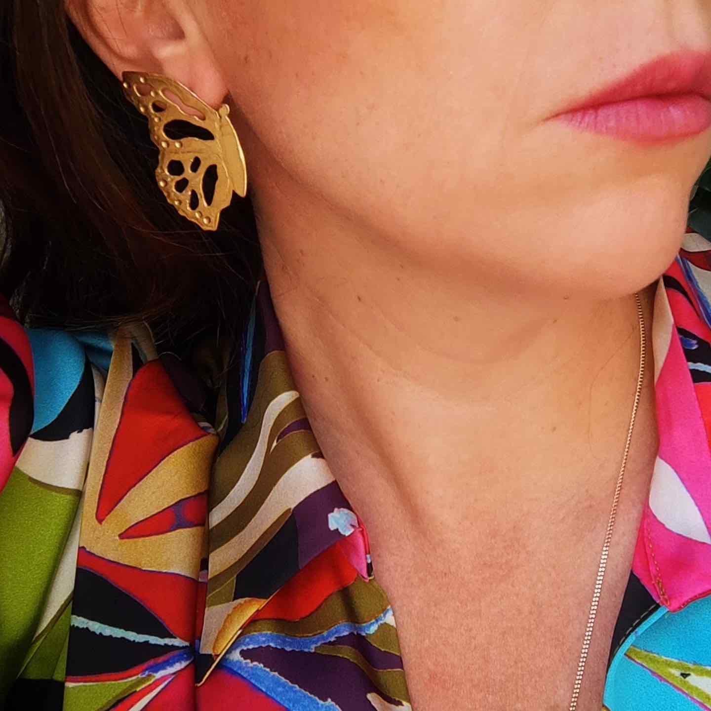 Pendientes de mariposa dorados, elegantes y modernos, combinados con blusa colorida de estampados vibrantes.
