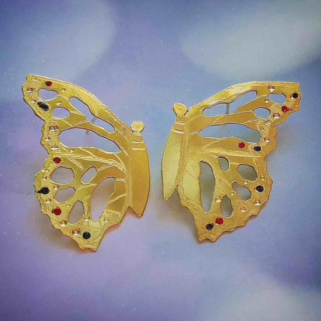 Pendientes mariposa dorados con detalles en rojo y negro, elaborados en metal, estilo elegante y moderno.