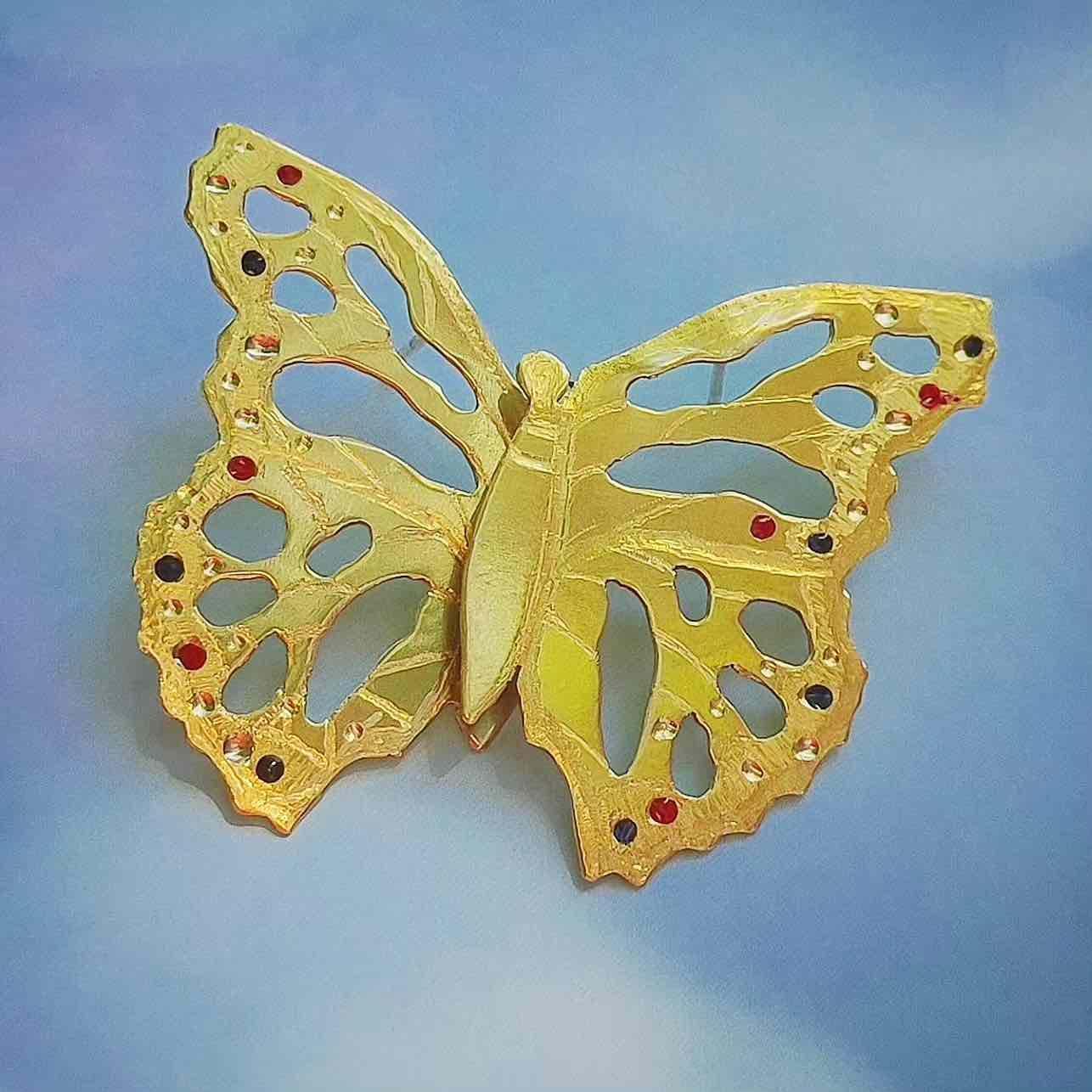 Broche de mariposa dorada con detalles en rojo, de metal, estilo elegante y moderno.