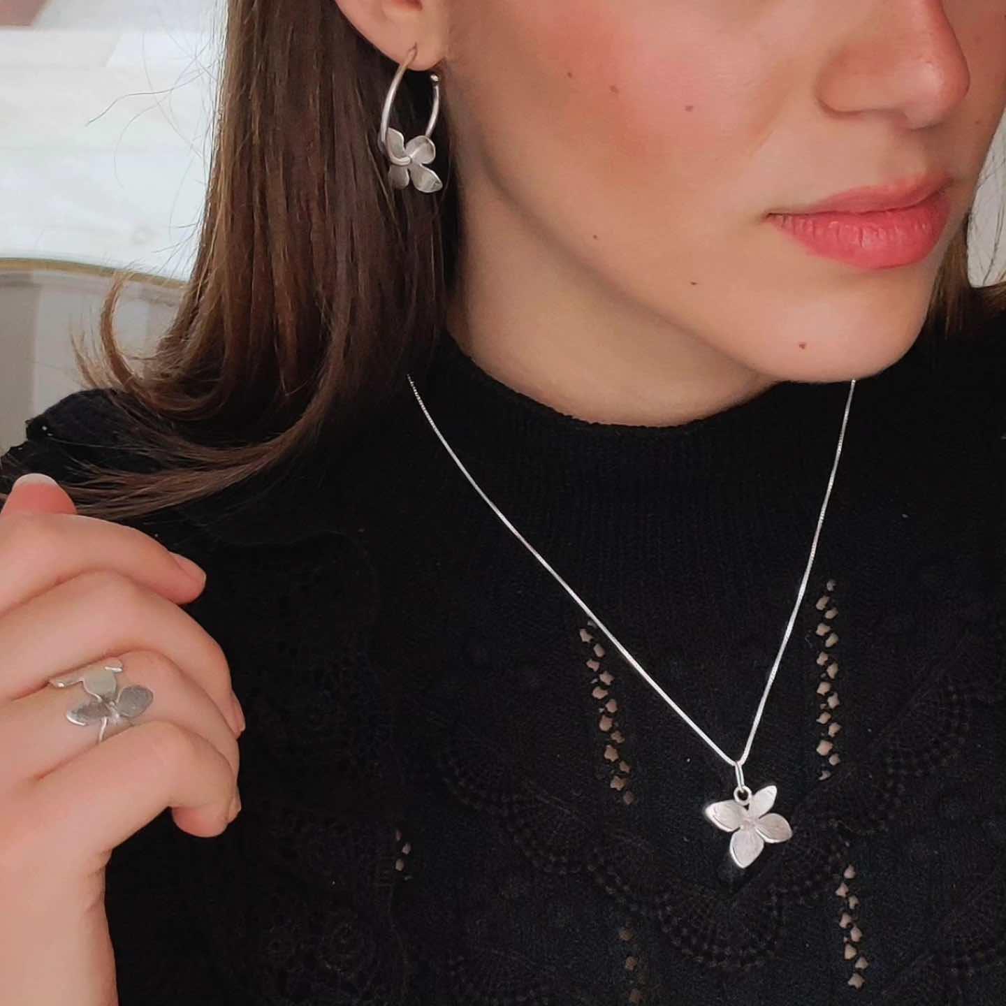 Conjunto de joyería de plata con diseño de flores, incluye pendientes, collar y anillo. Ideal para ocasiones especiales.