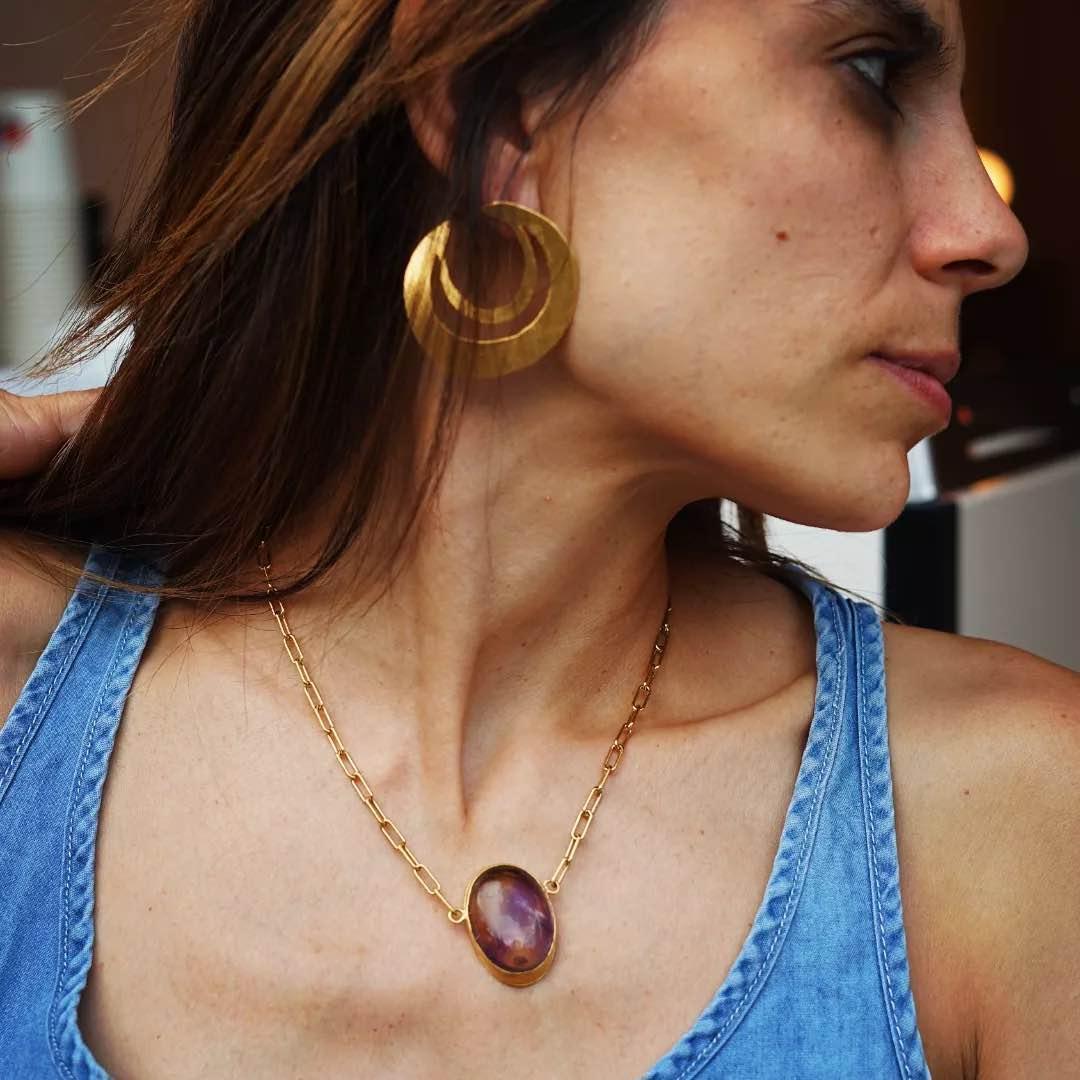 Collar dorado con ópalo púrpura y aretes circulares dorados, estilo bohemio y moderno.