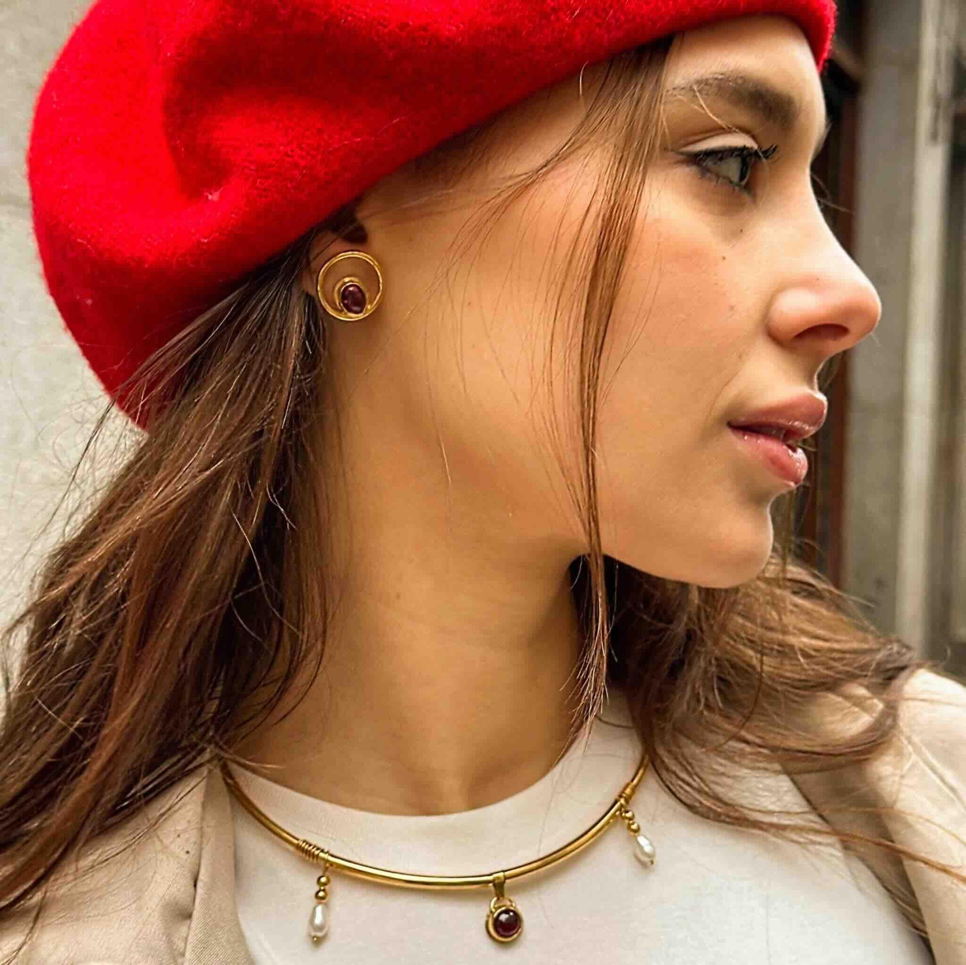 Collar dorado con perlas y pendientes de rubí, complementando un estilo elegante y moderno con boina roja.