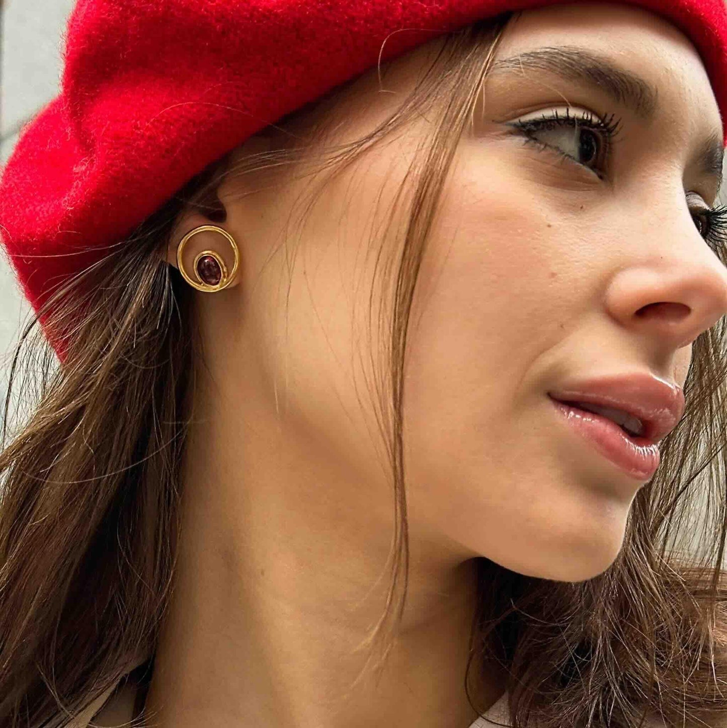 Pendientes dorados con ámbar, diseñados en estilo moderno, lucidos con un gorro rojo.