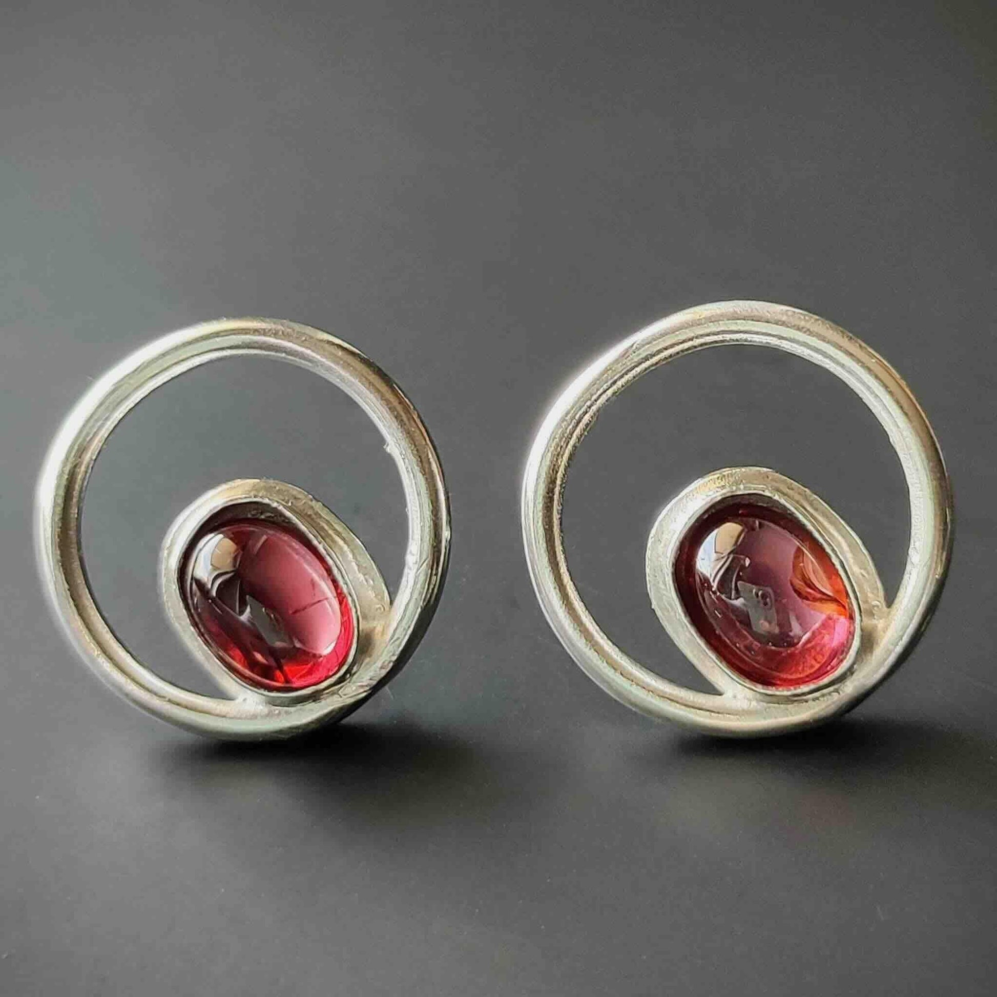 Pendientes de plata con diseño circular y piedras rojas, estilo moderno y elegante.