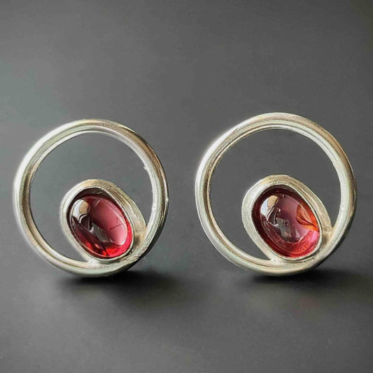 Pendientes de plata con diseño circular y piedras rojas, estilo moderno y elegante.