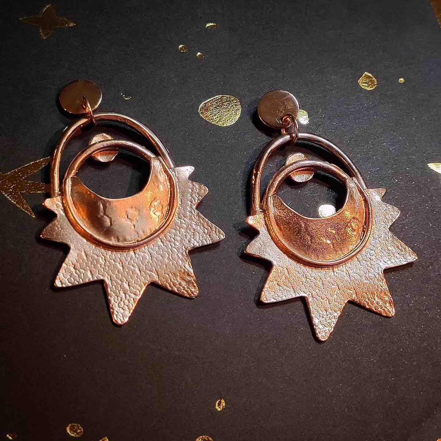 Pendientes de metal rosa con diseño de sol, brillante y texturizado, ideales para un estilo moderno y elegante.