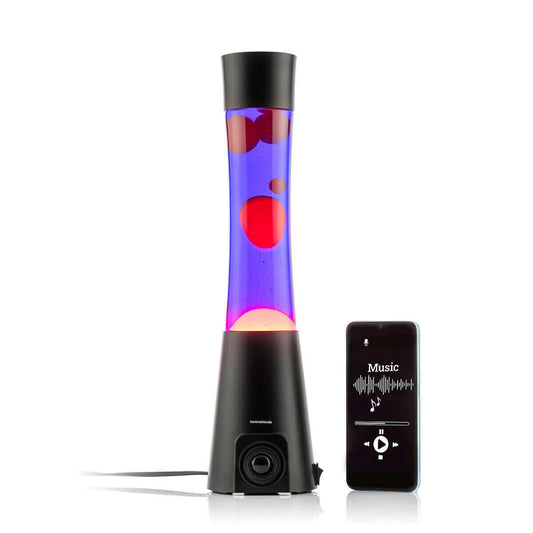 Lámpara de lava con base de altavoz negro, líquido morado y burbujas rojas junto a un smartphone reproduciendo música.