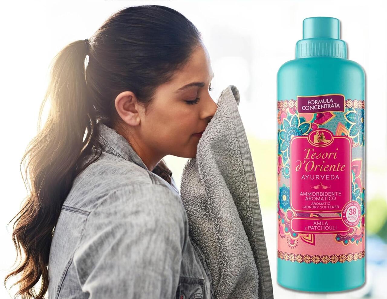 Mujer olfateando una toalla junto a una botella turquesa de suavizante concentrado con motivos florales coloridos.