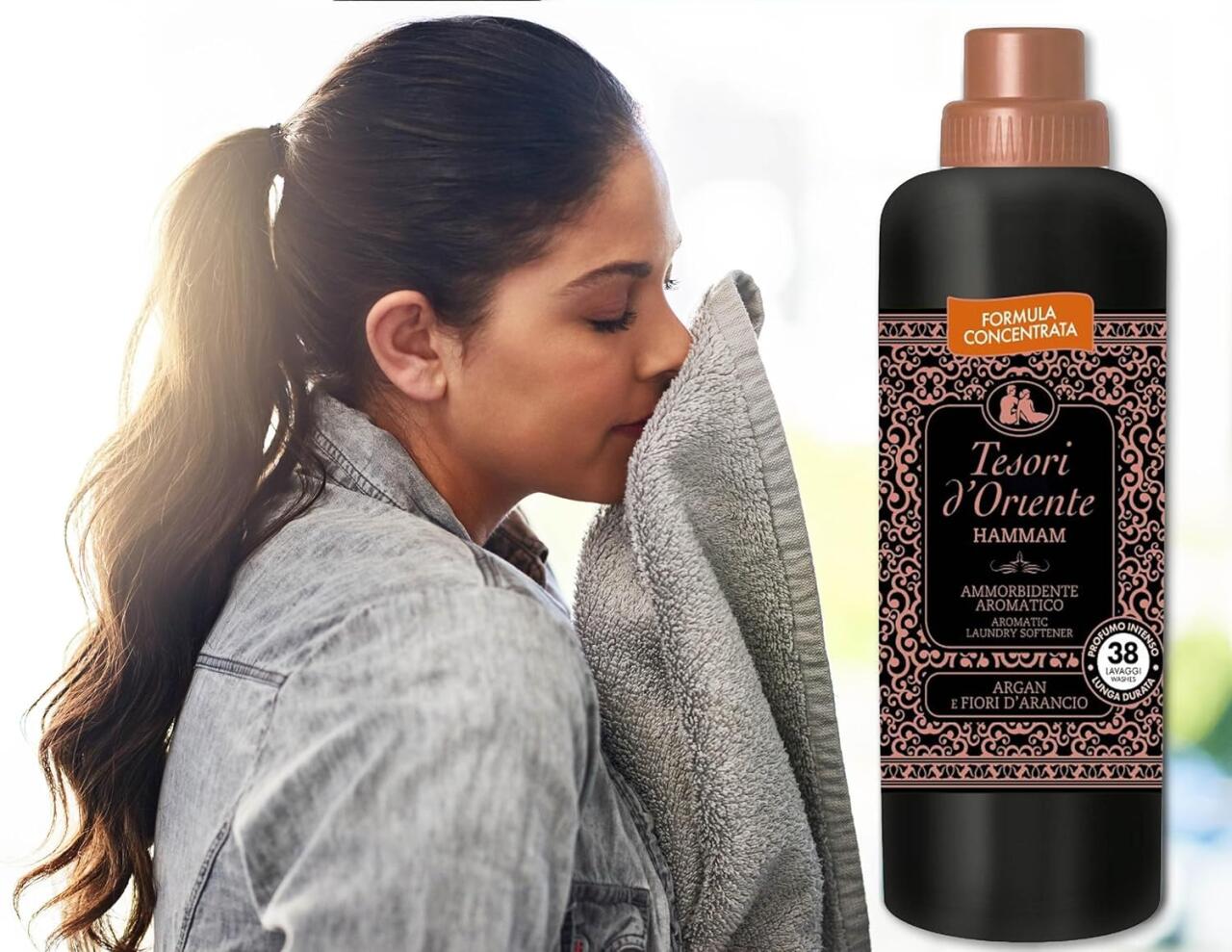 Mujer oliendo una toalla limpia junto a una botella negra de suavizante textil concentrado con diseño floral árabe.