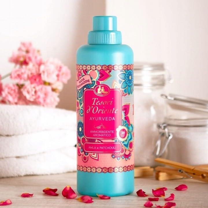 Botella de suavizante textil azul con diseño floral estilo árabe, rodeada de pétalos sobre una mesa blanca.