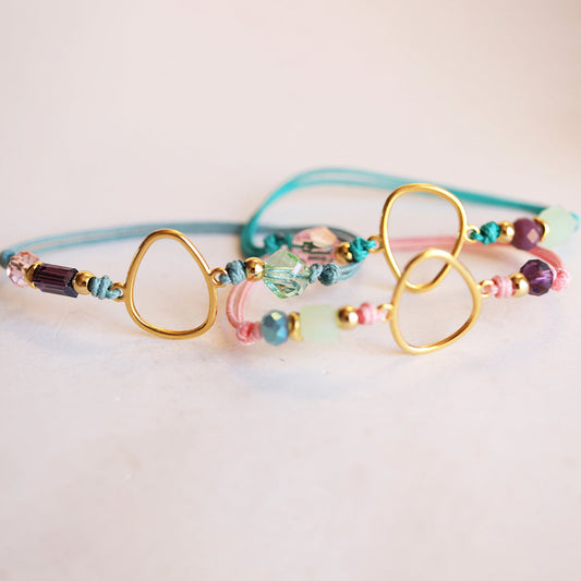 Pulsera de cuentas de cristal en tonos pastel, con detalles dorados y cordones de algodón en azul y rosa.