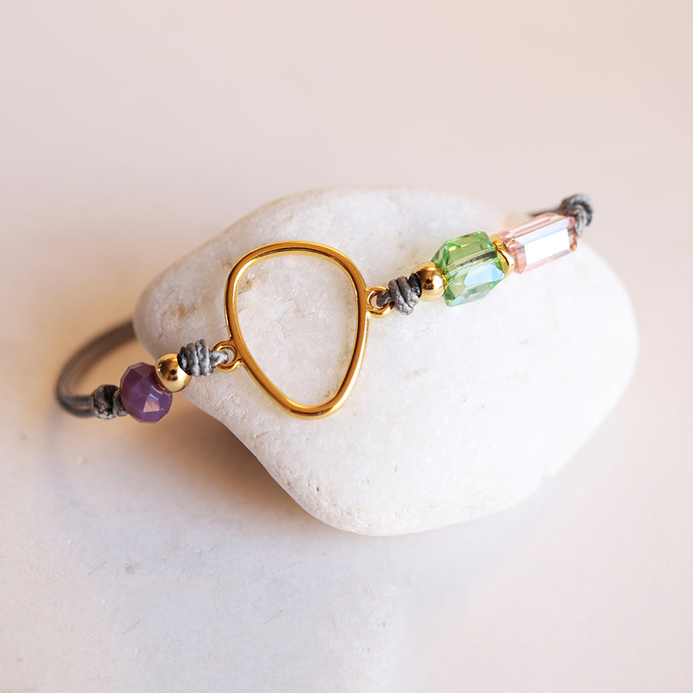 Pulsera elegante de hilo gris con piezas de cristal verde, púrpura y dorado en forma irregular.