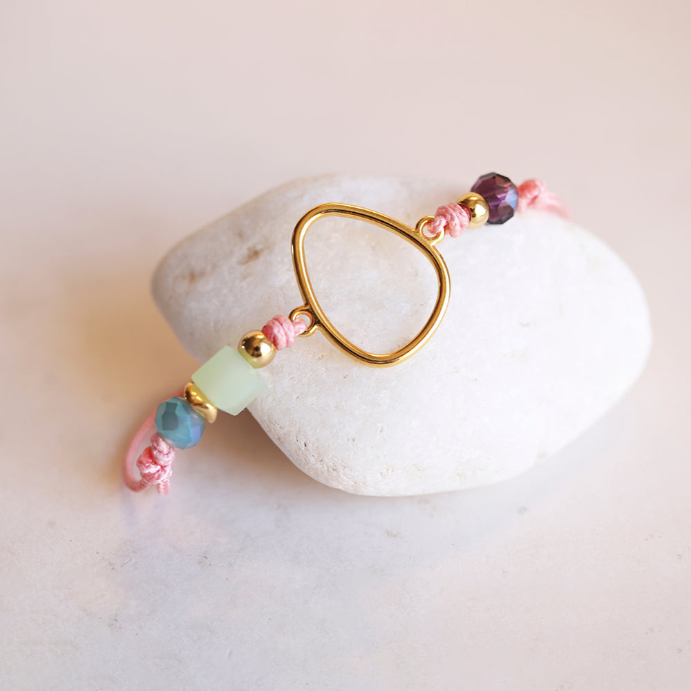 Pulsera artesanal rosa con cuentas de vidrio verde y morado, y detalle dorado en forma de gota.