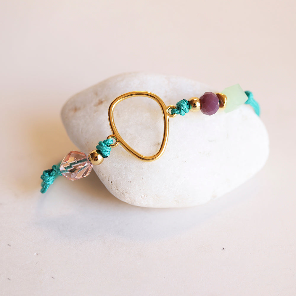 Pulsera artesanal de cuerda turquesa con detalles en oro y cuentas moradas y verdes, estilo bohemio.