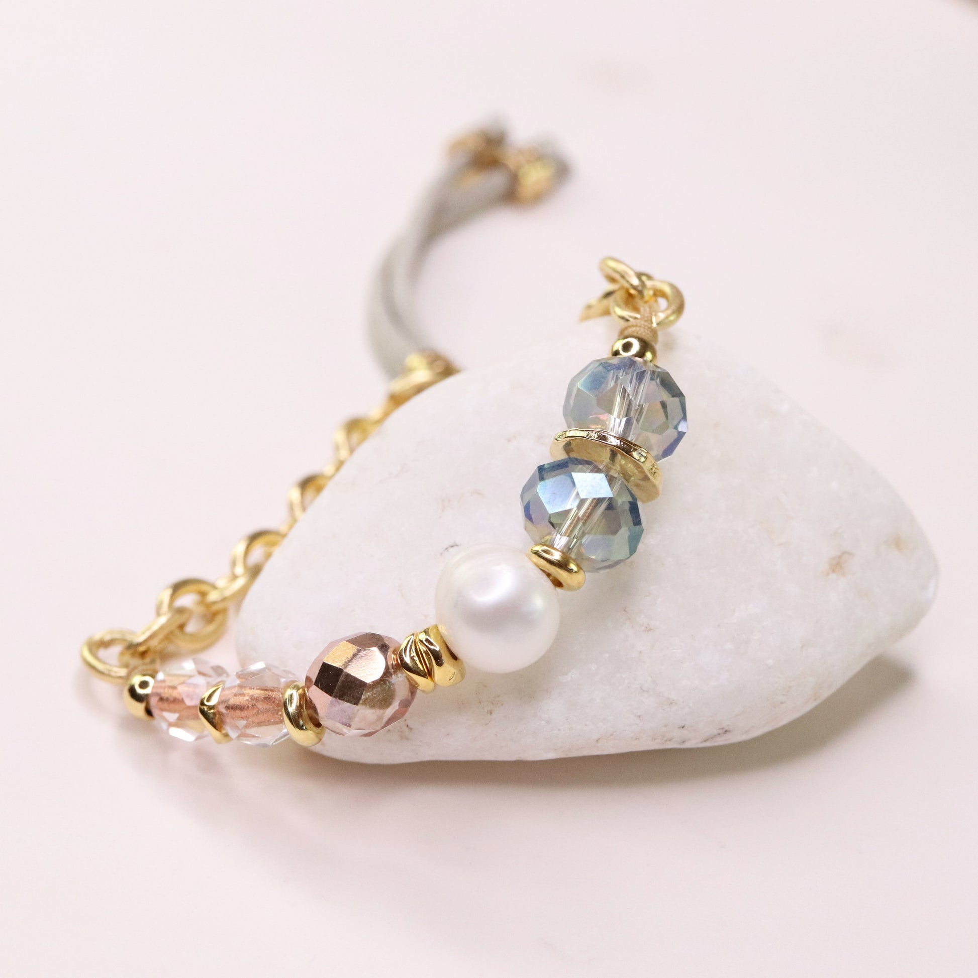 Pulsera de cuentas en tonos dorados, azules y rosas, con perla y cristal, estilo elegante y moderno.