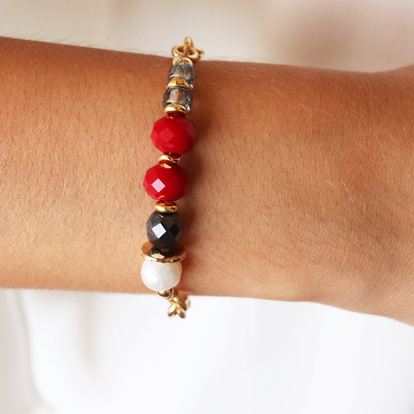 Pulsera de cuentas de cristal rojo, negro y perladas, con detalles dorados, estilo moderno y elegante.