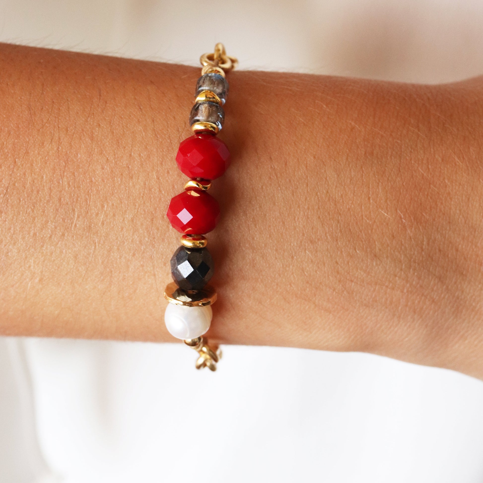 Pulsera de cuentas de cristal rojo, negro y perladas, con detalles dorados, estilo moderno y elegante.