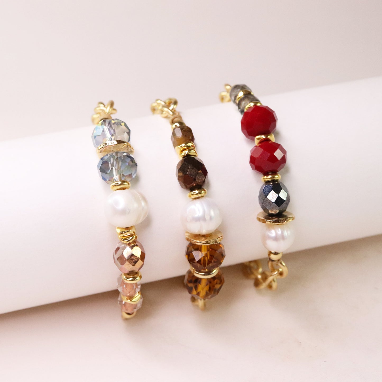 Pulseras trenzadas en oro, con cuentas de cristal azul, rojo y marrón, y perlas blancas. Estilo elegante y moderno.