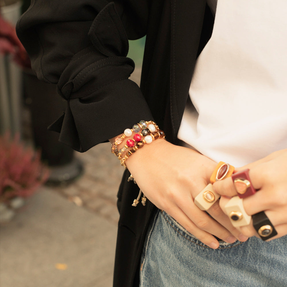 Pulsera de perlas multicolor con detalles dorados, estilo moderno, sobre una muñeca con anillos de diseño.