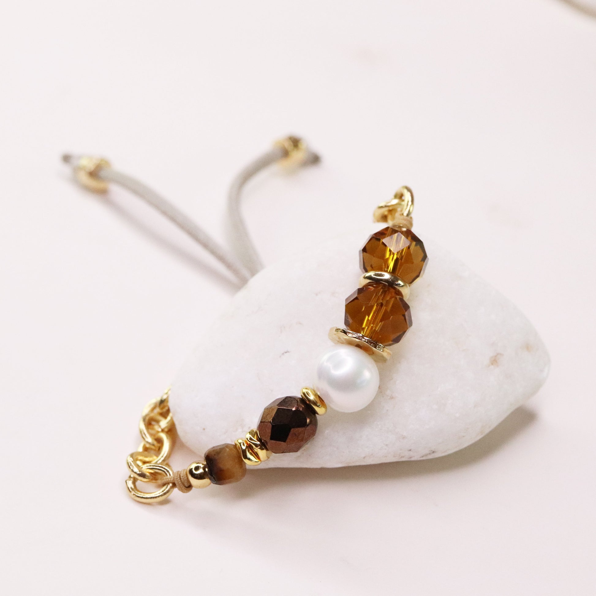 Pulsera elegante con cuentas de cristal ámbar, perla blanca y detalles dorados, sobre fondo de piedra blanca.