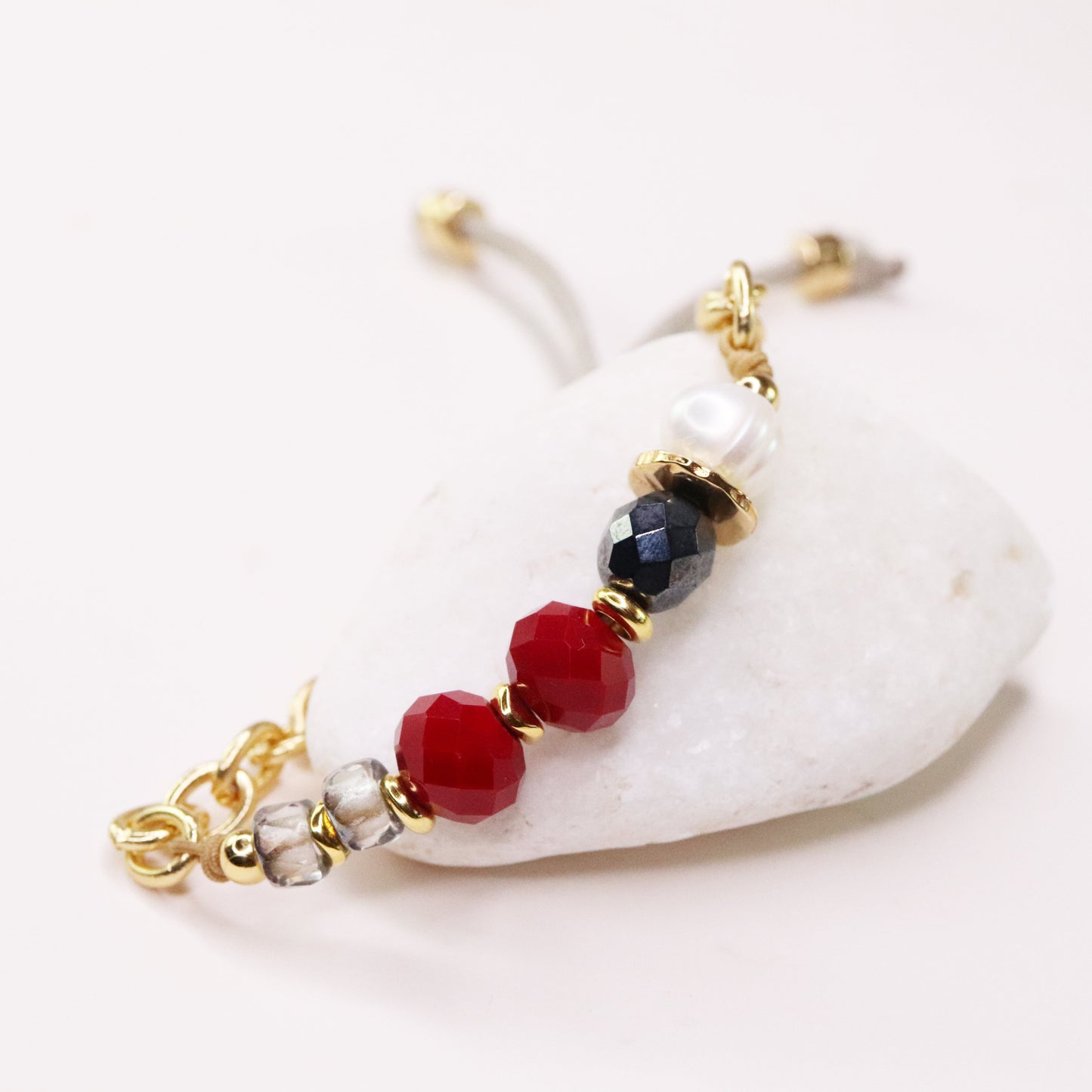 Pulsera de cuentas rojas, negras y perlas con detalles dorados, estilo elegante y moderno.