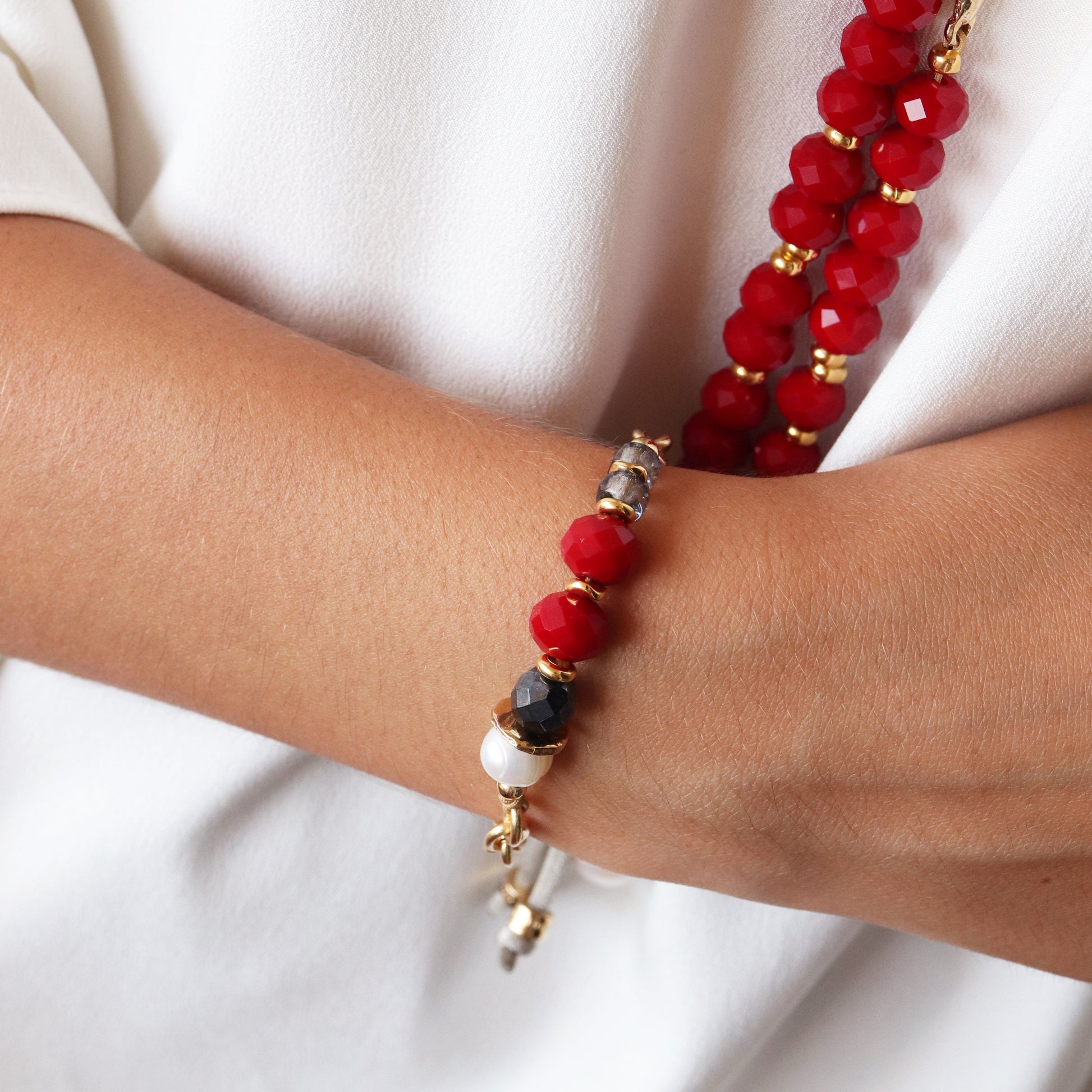 Brazalete de cuentas rojas y doradas, con detalles en negro y blanco, estilo bohemio y elegante.