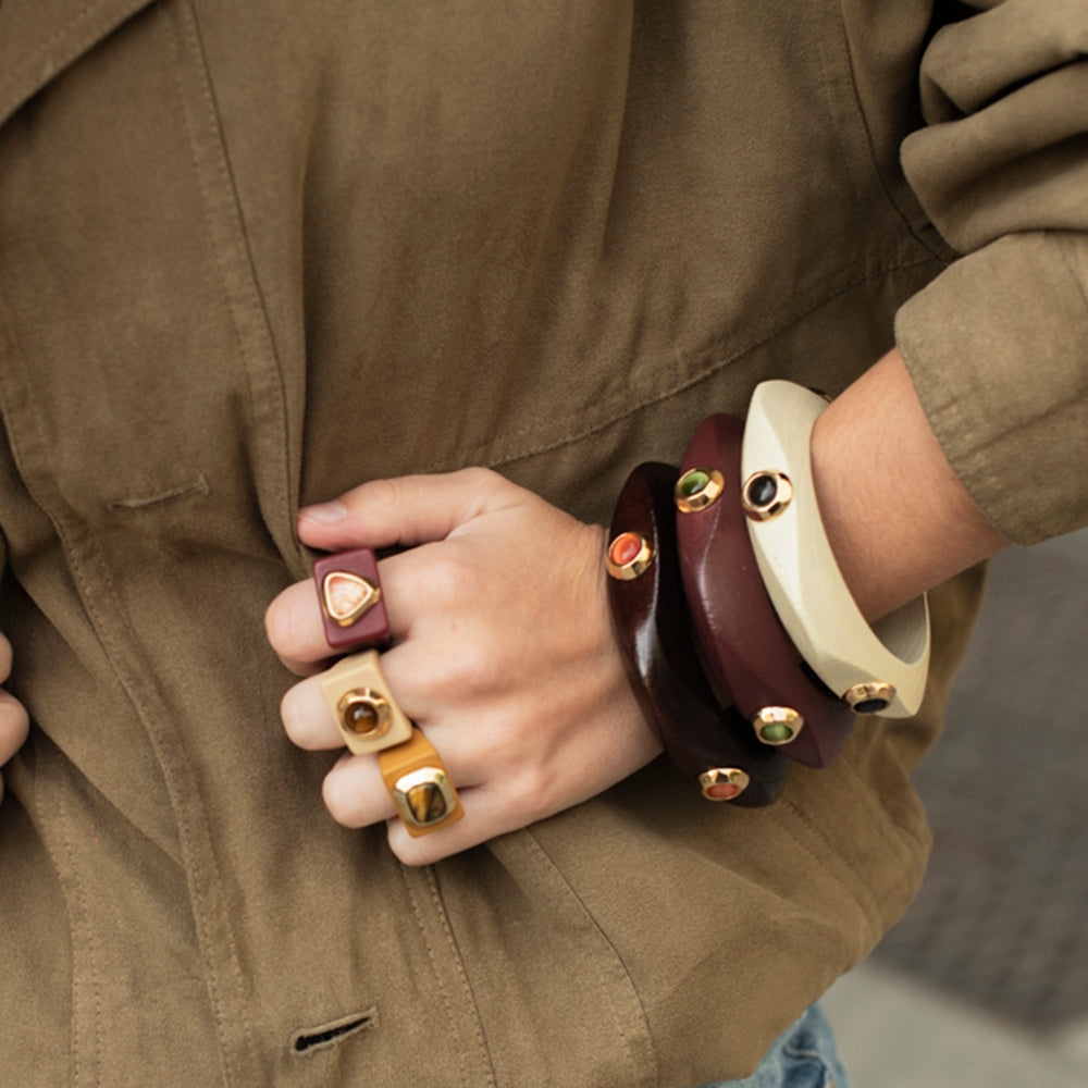 Pulseras y anillos de madera en tonos marrón y crema con detalles dorados, estilo moderno y elegante.
