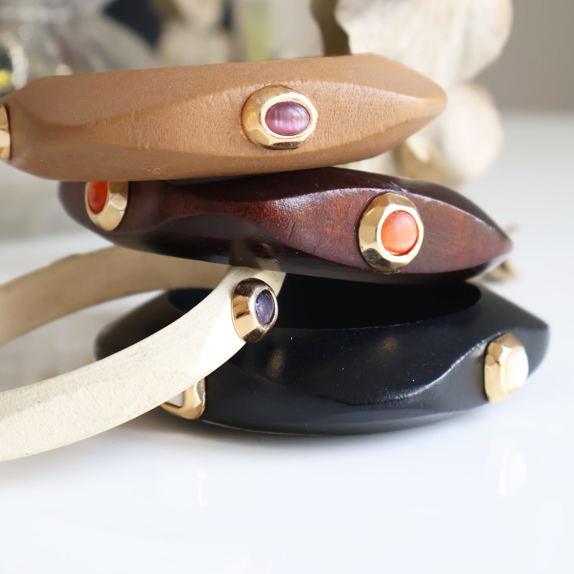 Pulseras de cuero en tonos beige, negro y marrón con detalles dorados y piedras de colores. Estilo elegante y moderno.