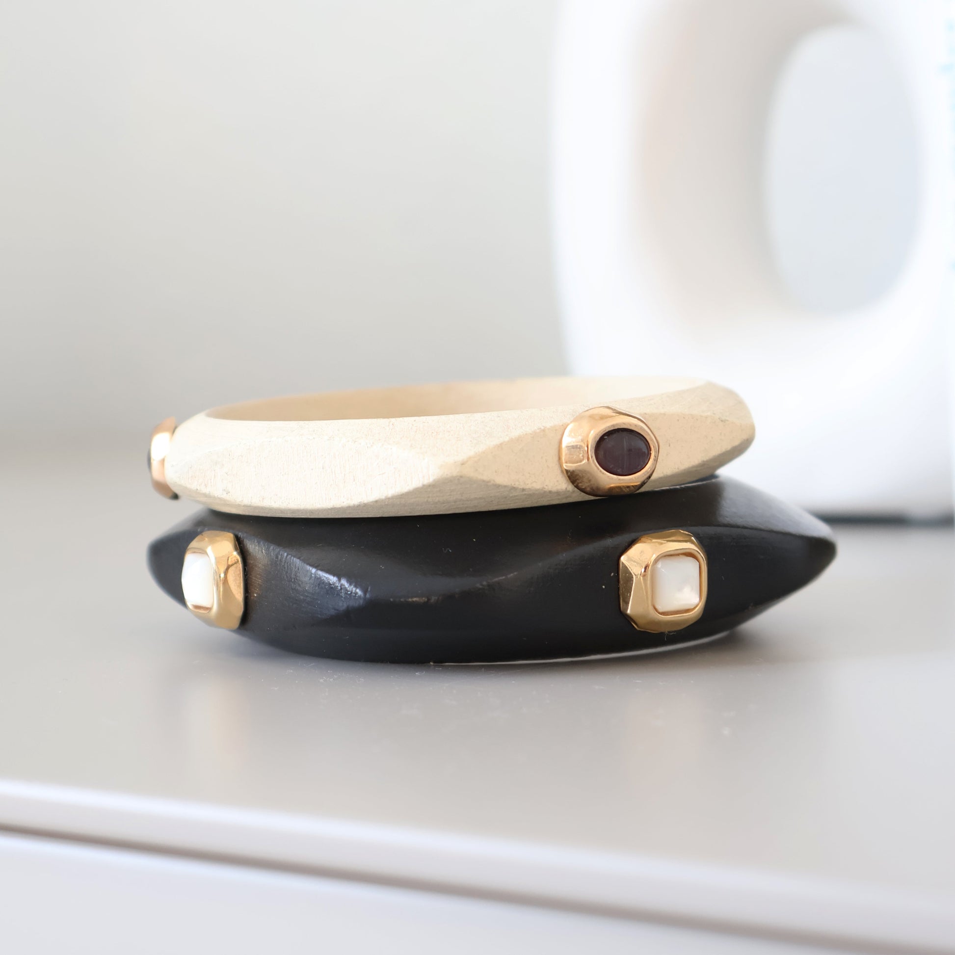 Pulsera de resina negra y beige con detalles dorados y piedras decorativas, estilo moderno y geométrico.