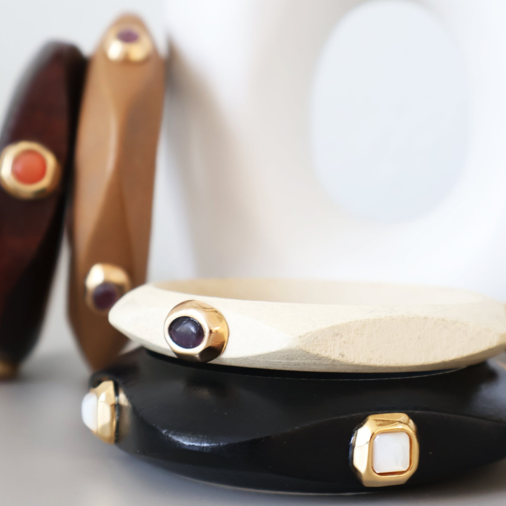 Brazaletes de madera en tonos negro, blanco, marrón y dorado, con detalles de piedras preciosas, estilo moderno y elegante.