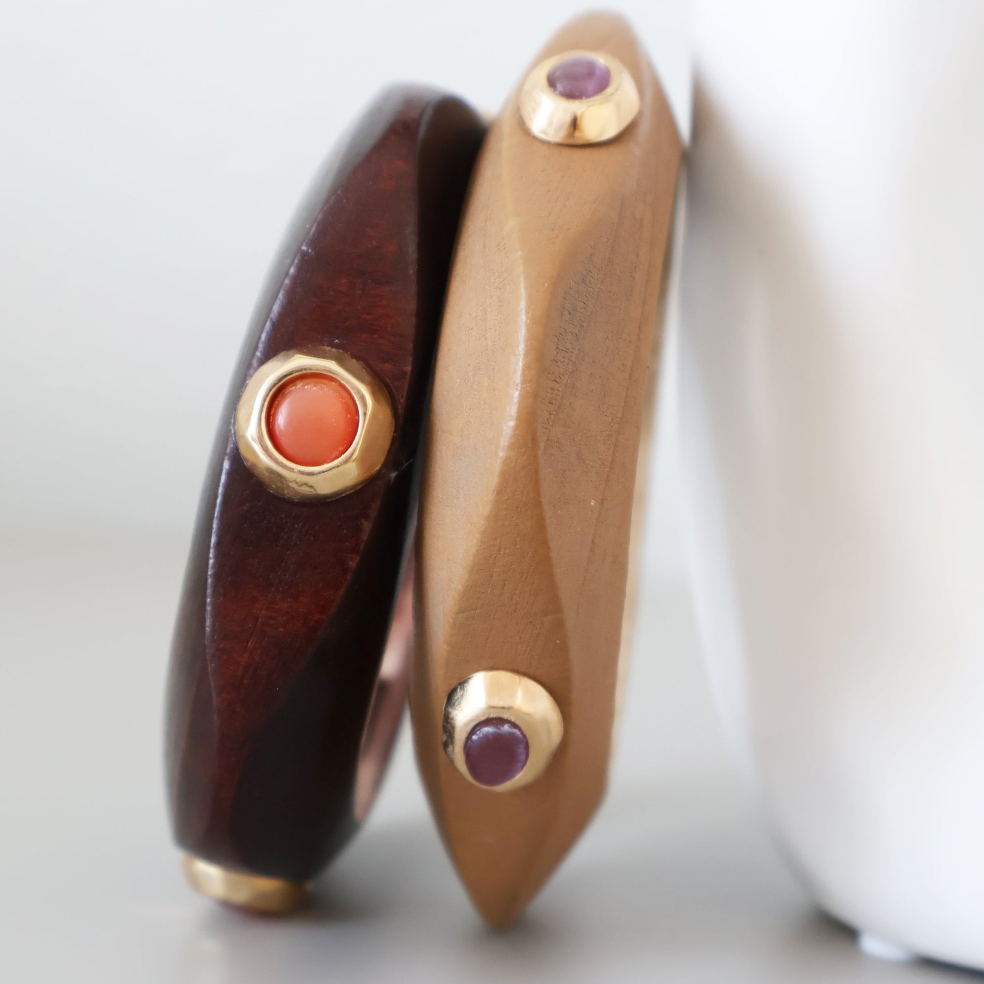 Pulseras de madera oscura y clara con detalles dorados y piedras rojas y moradas, estilo moderno y elegante.