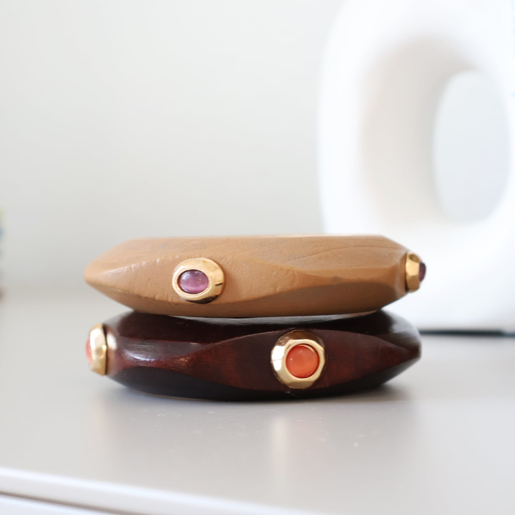 Pulseras de madera en tonos marrón y beige con gemas moradas y naranjas, estilo moderno y elegante.