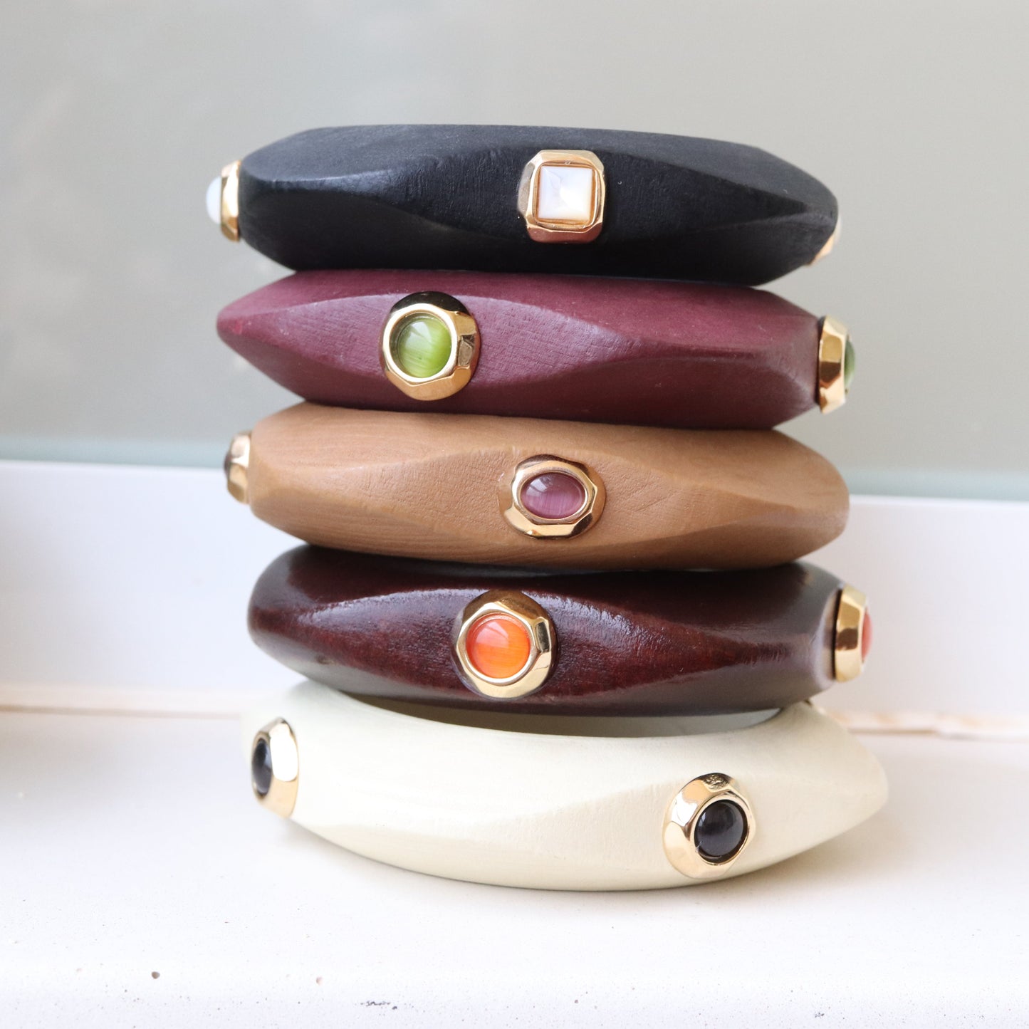 Pulseras de madera en tonos negro, marrón, beige, y burdeos con adornos dorados y piedras de colores.
