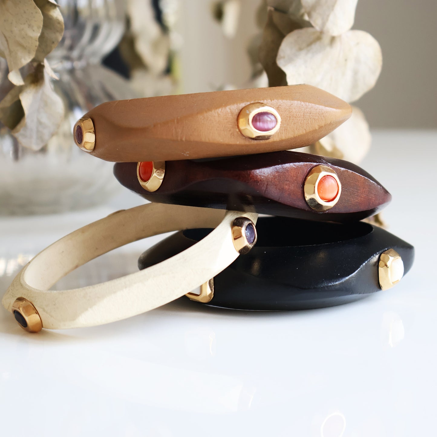 Brazaletes elegantes de cuero marrón, negro, blanco y madera con detalles en metal dorado y piedras de colores.