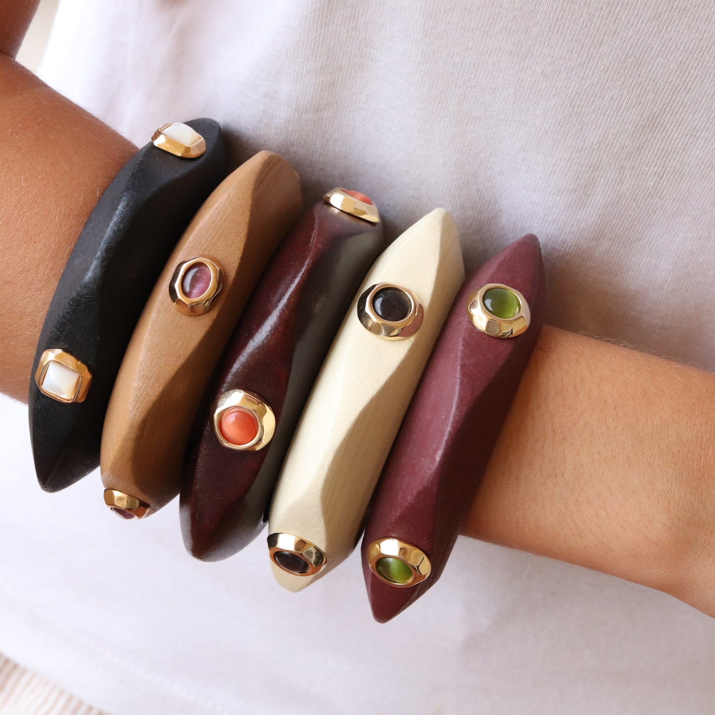 Pulseras de madera en tonos negro, marrón, burdeos y crema, con gemas de colores y detalles dorados.