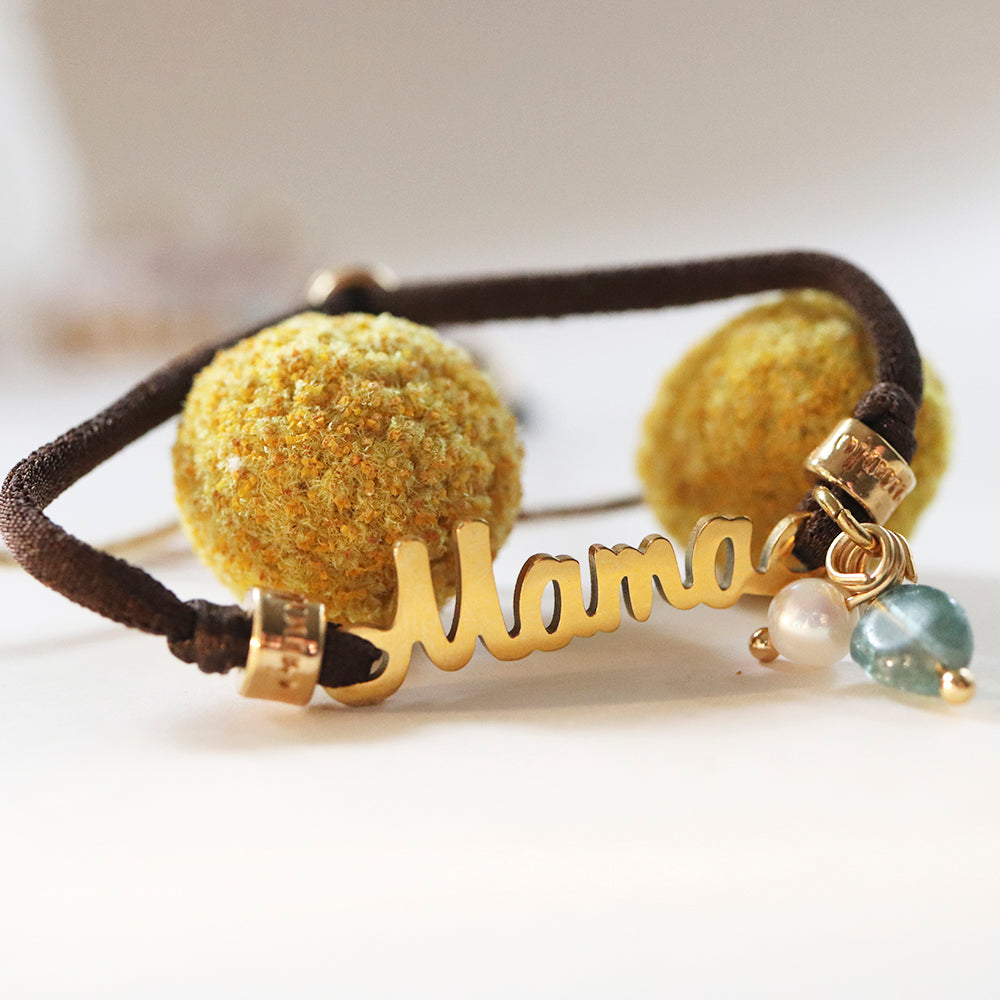 Pulsera personalizada "Mama" dorada con pompones amarillos y cuentas de vidrio en hilo marrón.