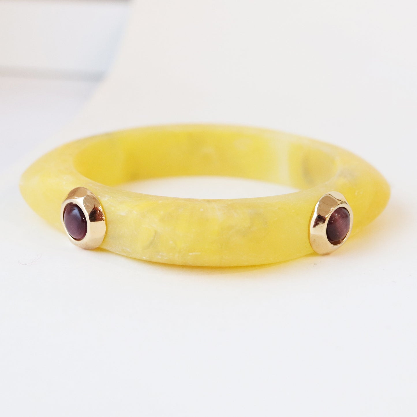 Pulsera de resina amarilla con detalles dorados y gemas moradas. Estilo moderno y elegante.