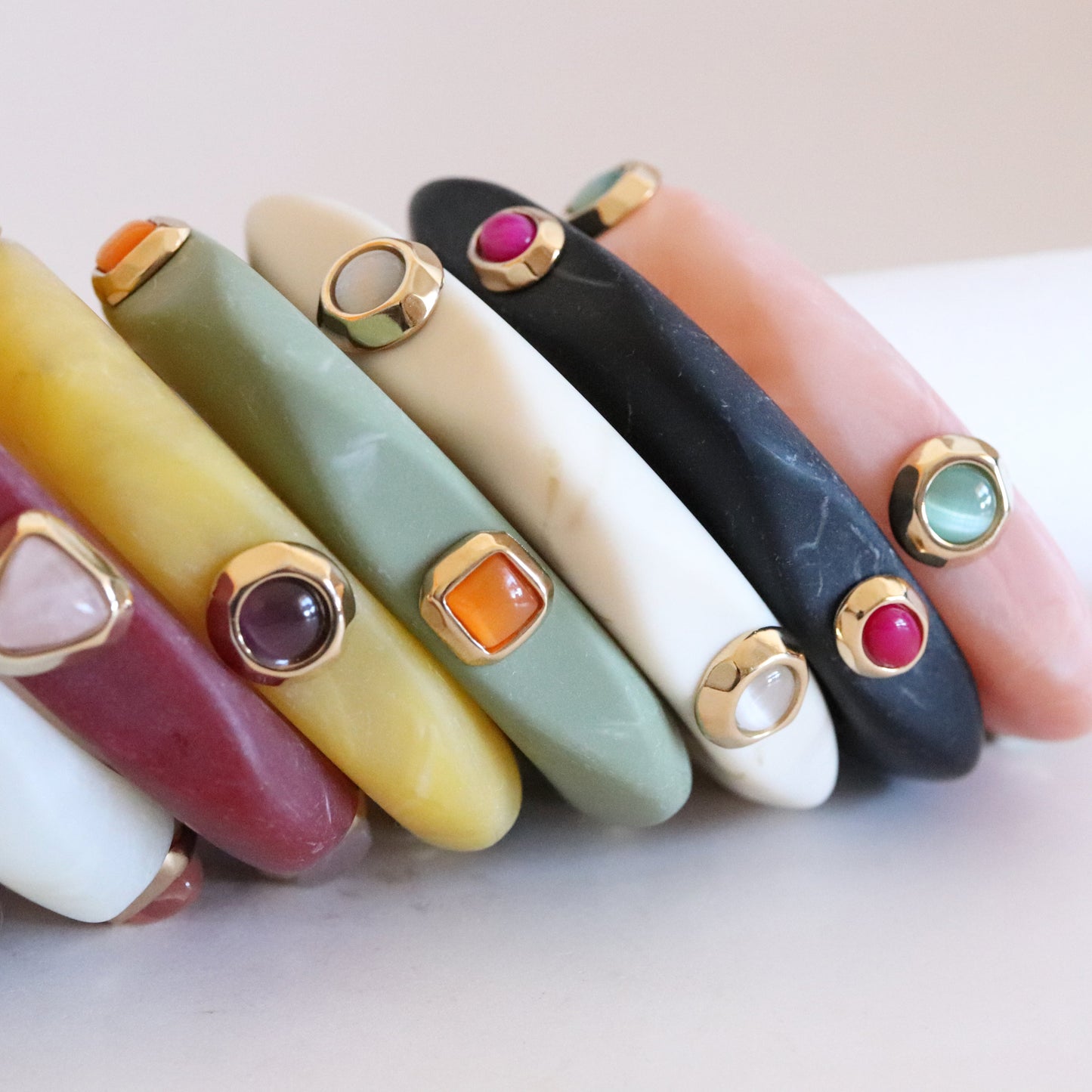 Brazaletes de resina en tonos pastel con detalles dorados y piedras de colores, estilo moderno y vibrante.