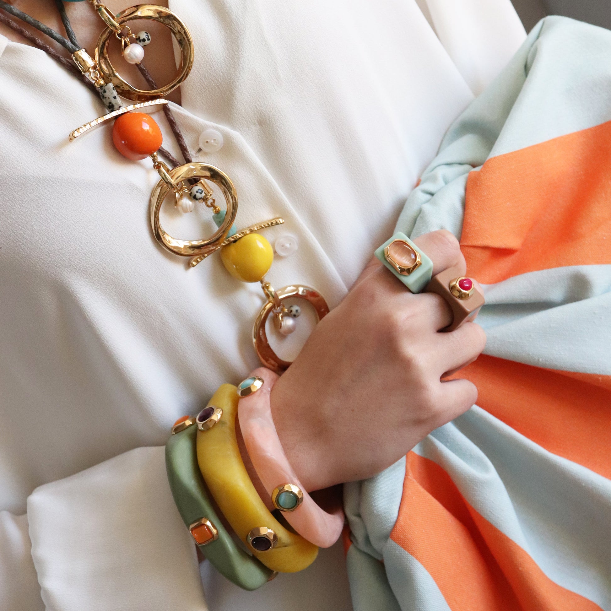 Collar dorado con cuentas de colores, pulseras en tonos pastel y anillo con piedra, estilo bohemio y moderno.