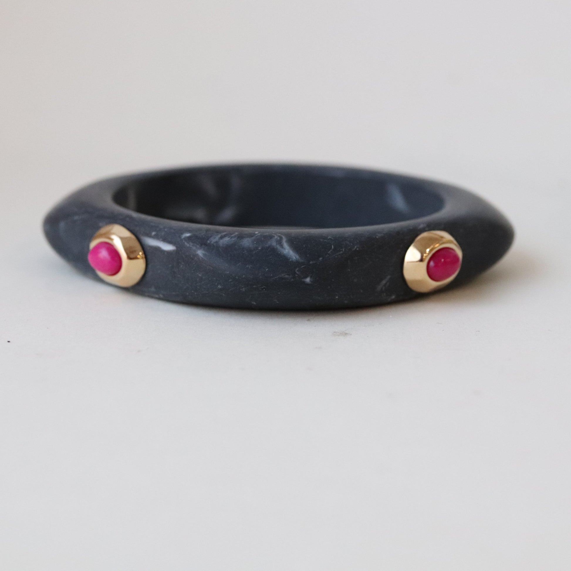 Brazalete de pizarra gris con detalles dorados y gemas rosa, estilo moderno y elegante.