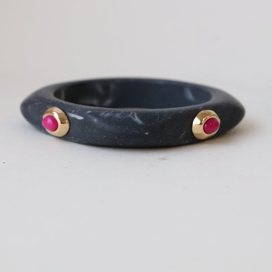 Brazalete de pizarra gris con detalles dorados y gemas rosa, estilo moderno y elegante.