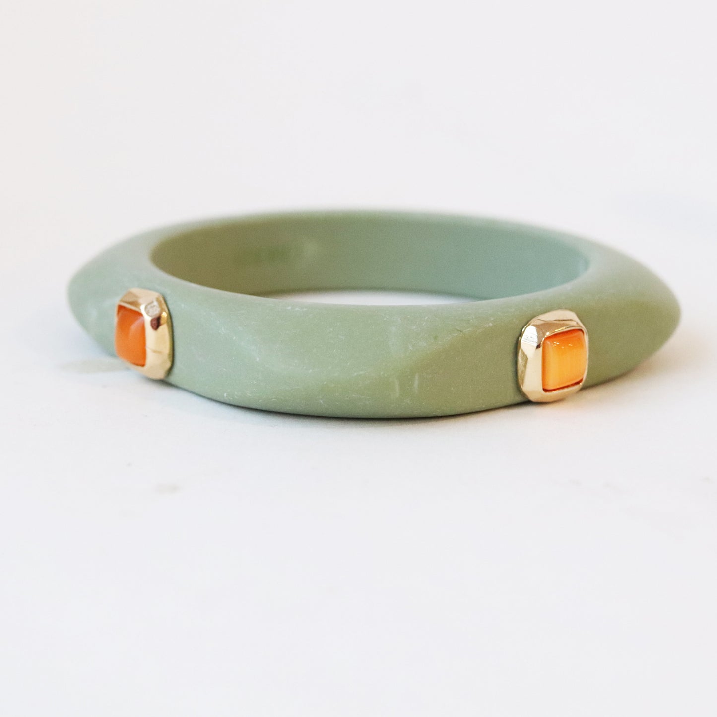 Pulsera de jade verde con detalles en oro y gemas rectangulares naranjas, estilo moderno y elegante.