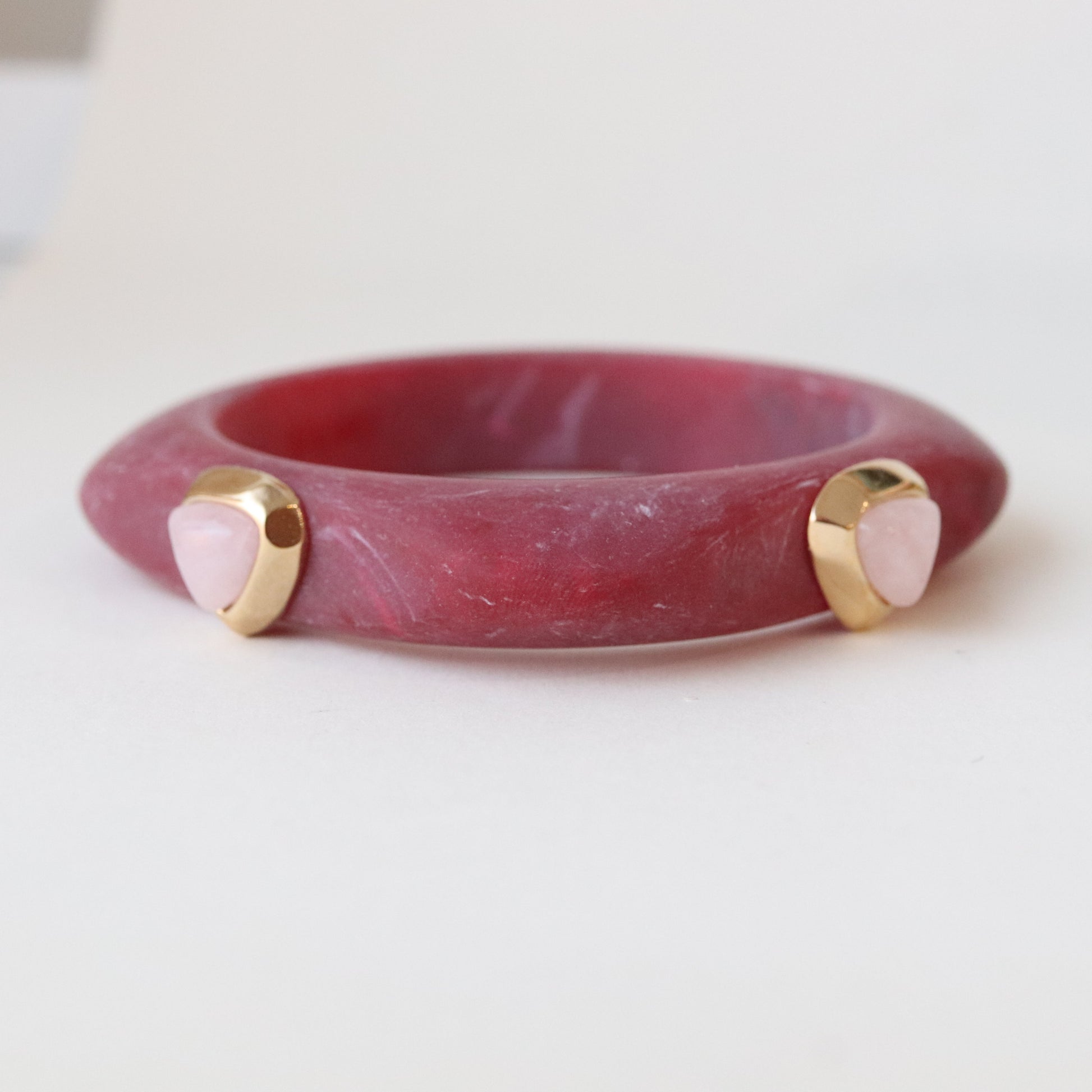 Brazalete de resina rosa con detalles dorados y piedras en forma de corazón, estilo moderno y elegante.