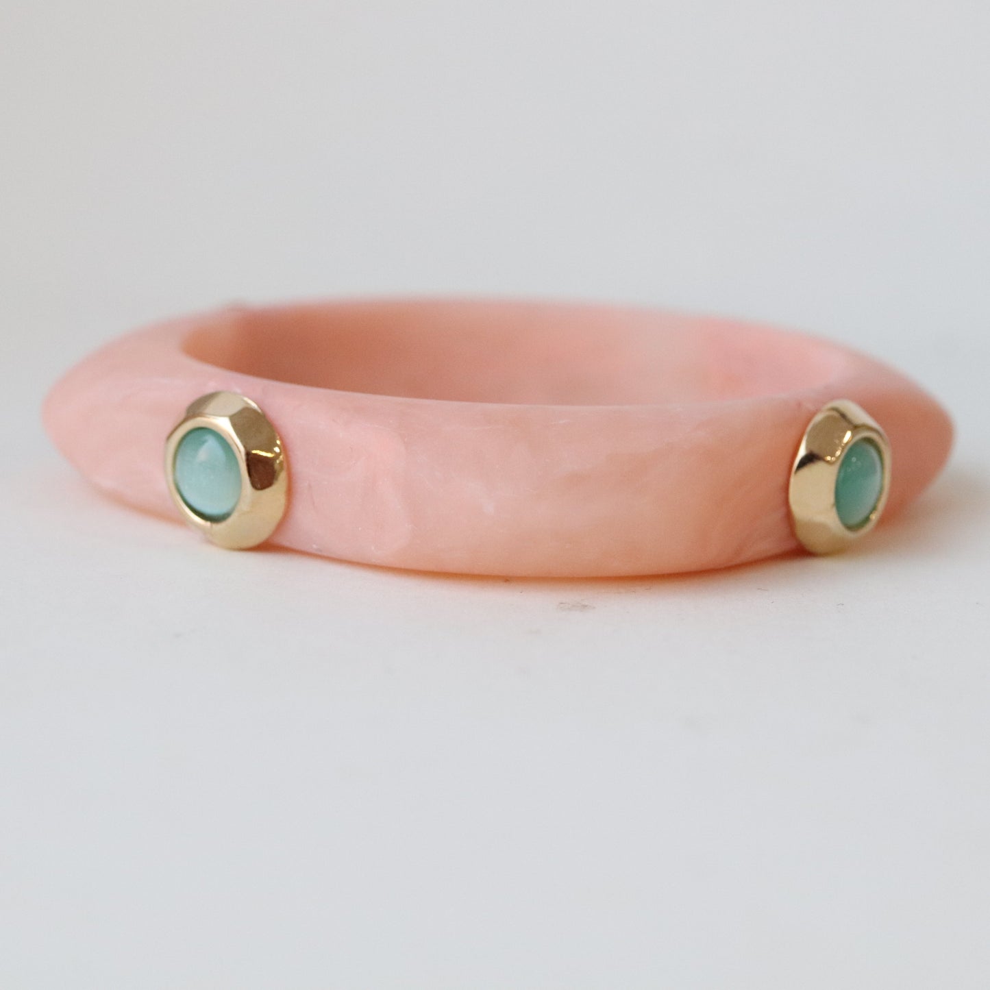Pulsera de resina color rosa con detalles dorados y piedras turquesas, estilo moderno y elegante.